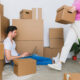 Crop woman arranging carton boxes during relocation with boyfriend using laptop on floor